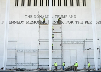 Workers stand on scaffolding near the signage for the Donald J. Trump and John F. Kennedy Memorial Center for the Performing Arts in Washington